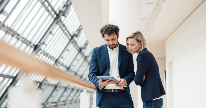 A man and woman are looking intently at a tablet the man is holding.