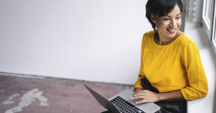 A woman holding a laptop is smiling while looking to her left.