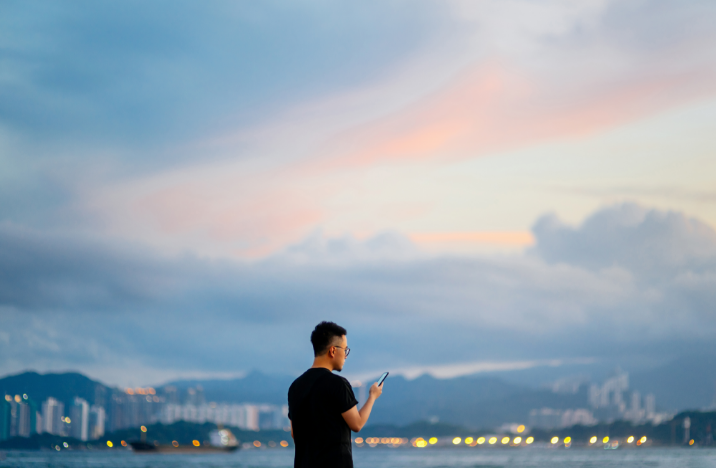 A man is using his phone. The background is a purple-pink skyline.
