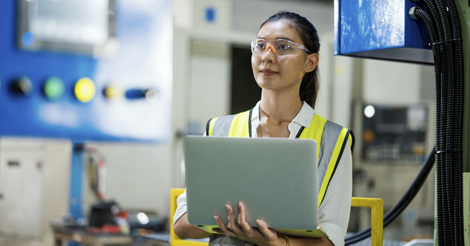 A woman in a safety jacket is holding a laptop.