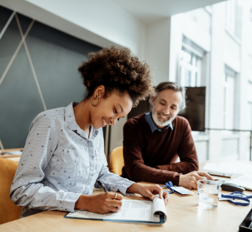 A woman is writing in a notepad while a man watches.