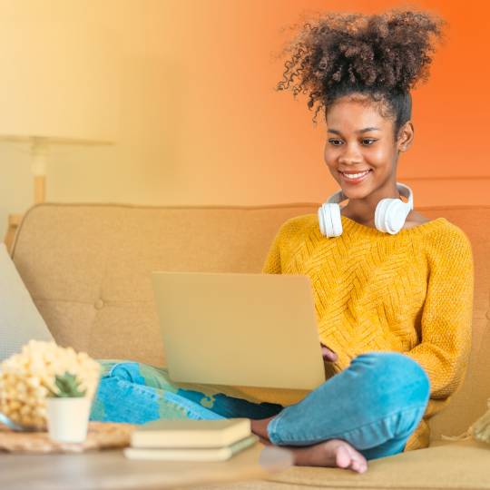 A woman is sitting on a couch looking at the laptop on her lap.