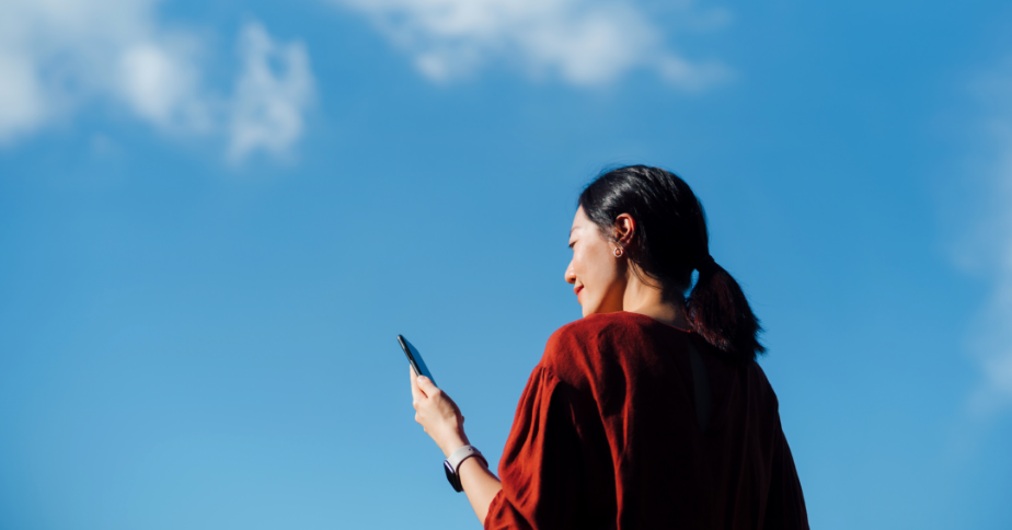 A woman is outside in an open area, looking at her phone.