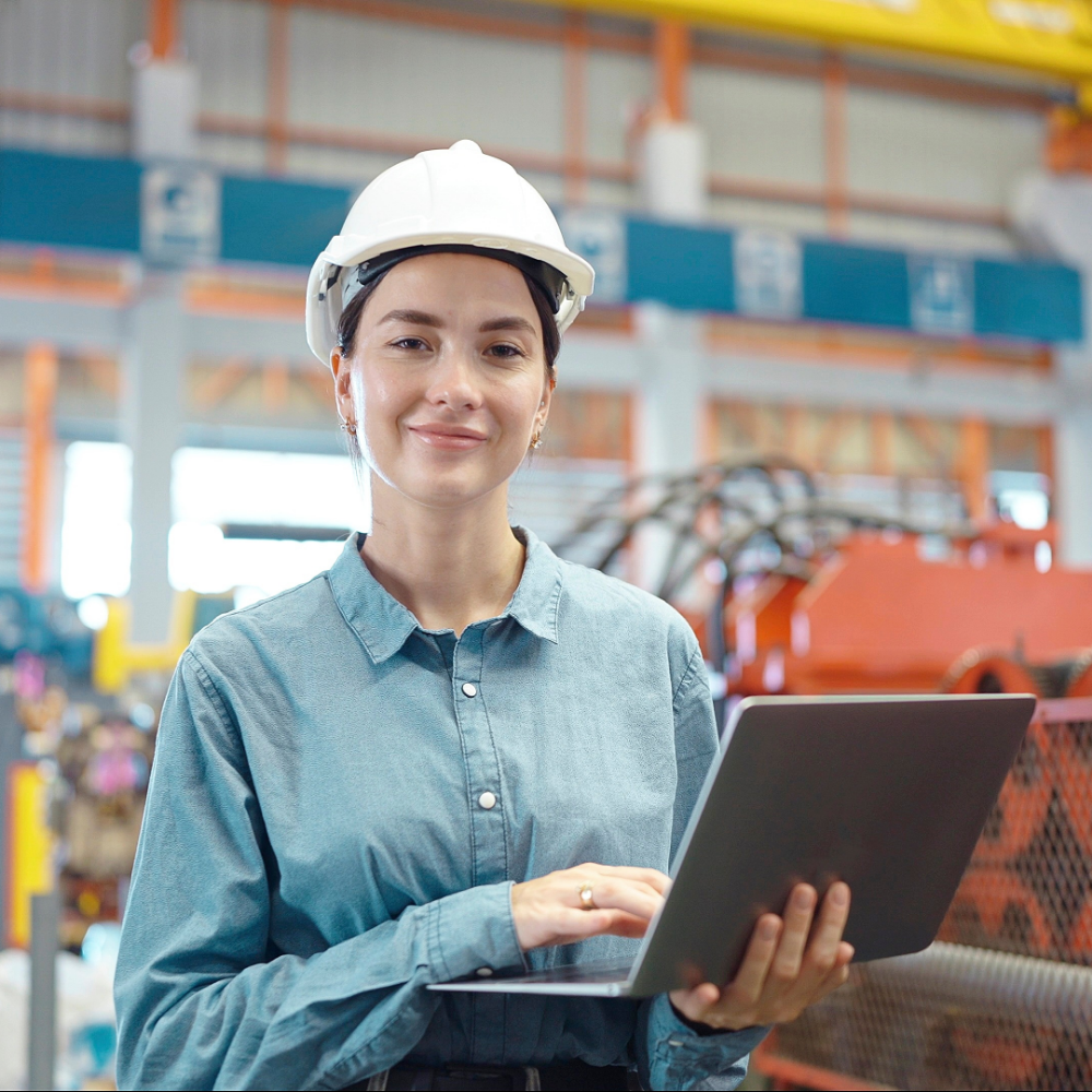 A woman is holding a laptop and smiling while looking ahead.