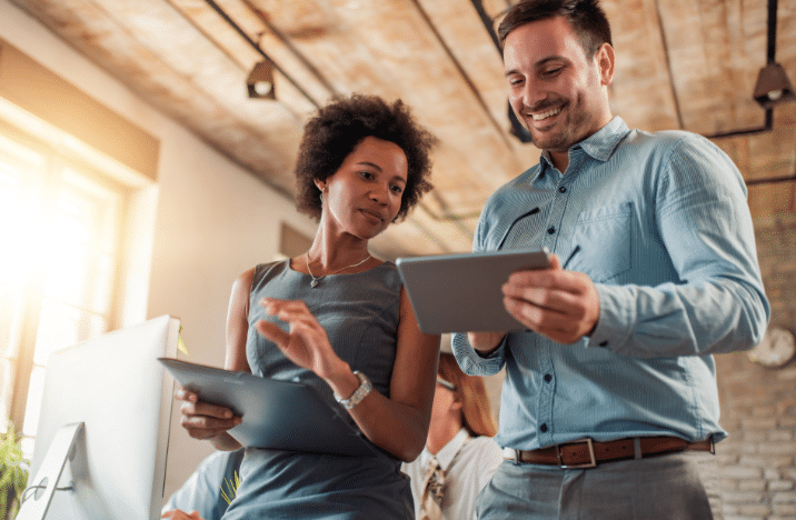 A man and woman are looking at a tablet the man is holding.